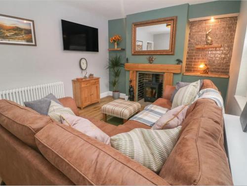 a living room with a brown couch and a fireplace at Sunshine Cottage Tideswell, Games room included. in Tideswell