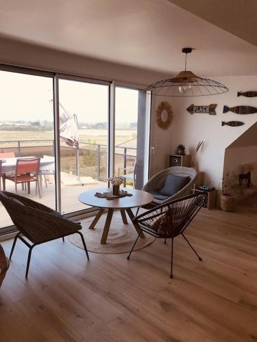 un salon avec une table, des chaises et des fenêtres dans l'établissement Ker-Lina sea view, calm guaranteed, à Plounévez-Lochrist