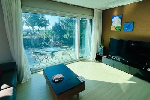 uma sala de estar com uma grande janela e uma televisão em Areumdaumga Pension em Seogwipo