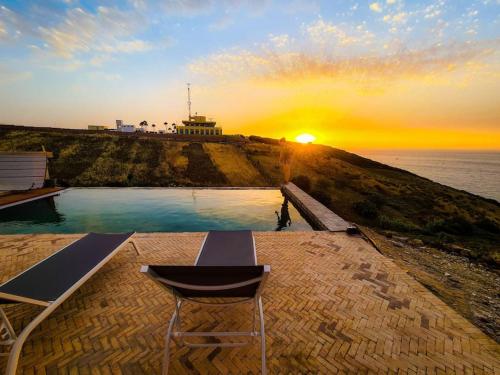 a chair sitting in front of a pool with the sunset at Très belle villa avec piscine et vue incroyable sur mediterannée (DAR NAIM) in Tangier