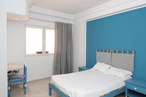 Dormitorio azul y blanco con cama y ventana en NARCISSE RESIDENCE, en Hammam Sousse