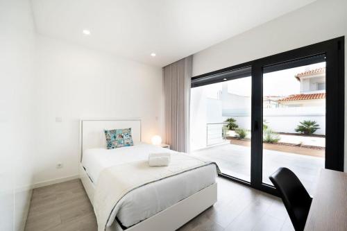 a white bedroom with a bed and a large window at Villa Nazaré - Pool, BBQ and Boule/Petanque in Nazaré