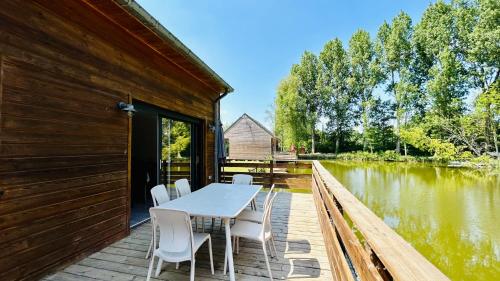 Chalet avec terrasse sur pilotis vue sur l'étang في رو: طاولة وكراسي على سطح بجوار نهر