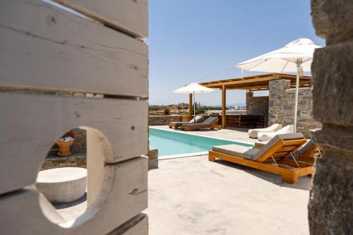 a pool with lounge chairs and an umbrella next to a house at Cycladic Breeze Villas in Kampos Paros