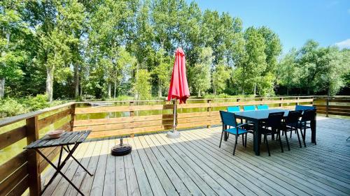 a wooden deck with a table and chairs and an umbrella at Chalet avec terrasse sur pilotis vue sur l'étang in Rue