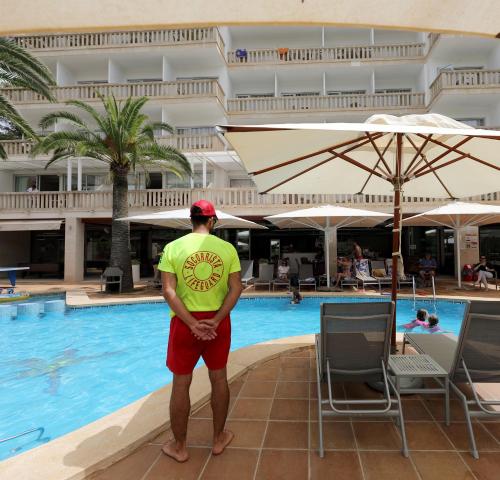 a man standing in front of a swimming pool at Hotel Apartamentos Cala Santanyi in Cala Santanyi