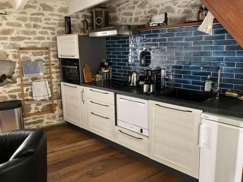 une cuisine avec des placards blancs et un mur en briques bleues dans l'établissement Petite maison de pêcheur, à l'Île-aux-Moines