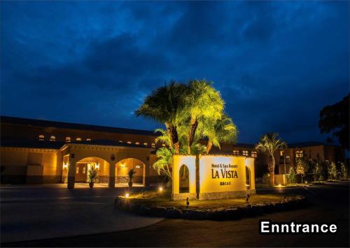 a building with a sign and palm trees at night at La Vista Kirishima Hills in Kirishima