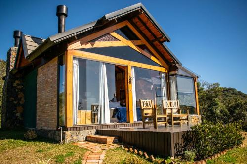 a cabin with a large glass door and two chairs at Caminho das Nuvens - Cabanas de Montanha in Bom Retiro