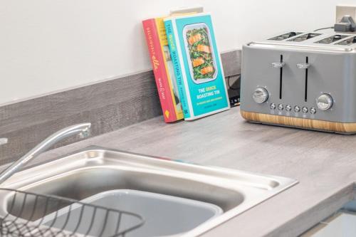 a kitchen counter with a sink and a toaster and books at The Winnoch - modern 2 bed flat in Lochwinnoch