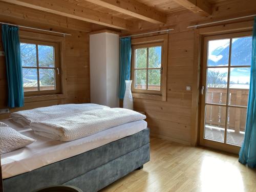a bedroom with a bed with blue curtains and windows at Chalet Descansa in Neukirchen am Großvenediger