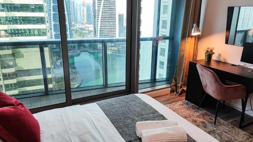 a bedroom with a bed and a desk and a large window at La Buena Vida Holiday Homes - Luxe 1BD, boutique apt full lakeview 1m to Metro, Lake & Almas Tower in Dubai