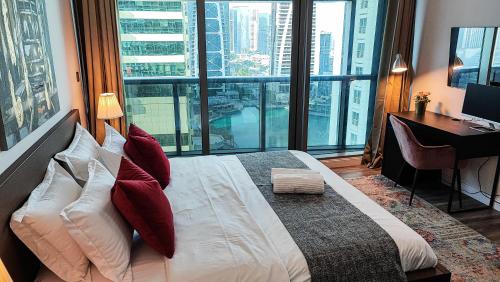 a bedroom with a large bed with a desk and windows at La Buena Vida Holiday Homes - Luxe 1BD, boutique apt full lakeview 1m to Metro, Lake & Almas Tower in Dubai