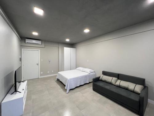 a bedroom with a bed and a couch and a tv at Studio Residencial no coração do 4° Distrito in Porto Alegre