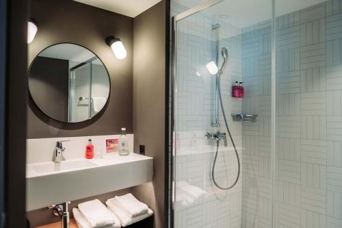 uma casa de banho com um chuveiro, um lavatório e um espelho. em Moxy Sion em Sion