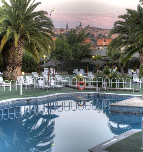 a swimming pool with palm trees and a city in the background at Beatriz Toledo Auditorium & Spa in Toledo
