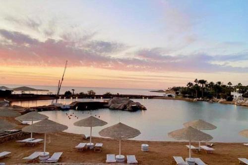 Domina Coral Bay Resort &casino في Dawwār Ruḩayyim: حمام سباحة مع مظلات وكراسي والمحيط