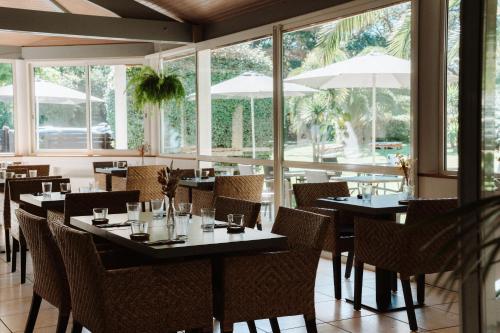 un comedor con mesas, sillas y ventanas en Hôtel Les Fougères, en Hossegor