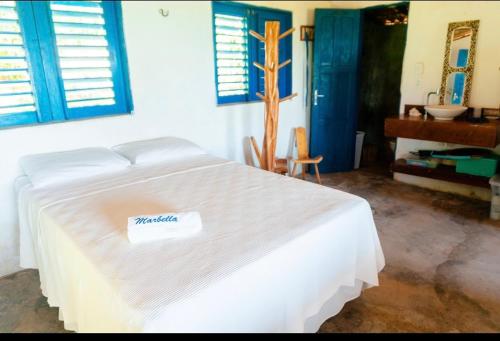 1 cama blanca en un dormitorio con ventanas con persianas azules en Pousada Estrela Peroba, en Icapuí