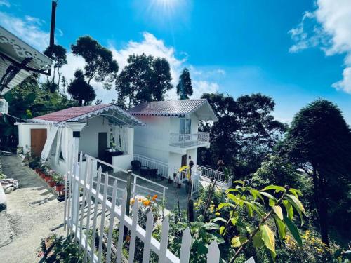 a white house with a white fence and trees at K - Den Homestay in Kurseong