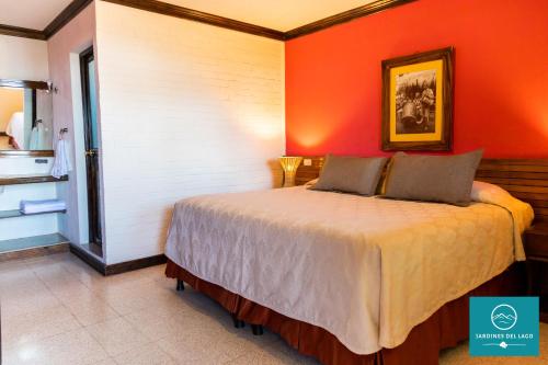 a bedroom with a bed with an orange wall at Hotel y Centro de Convenciones Jardines del Lago in Panajachel