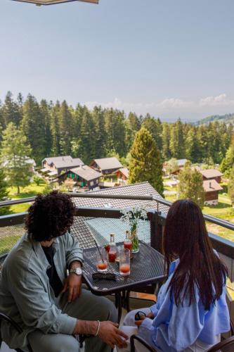 a man and a woman sitting at a table on a balcony at Boutique hôtel Corbetta - SPA 60m2 - La montagne à 5 minutes de l'autoroute A12 aux Paccots sur Montreux - NOUVEAU Loft familial - Profitez du Lac Léman et des montagnes en même temps in Les Paccots