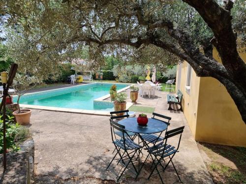 a table and chairs under a tree next to a pool at Gîte avec Piscine au cœur de la Vallée de la Cèze in Saint-Laurent-de-Carnols