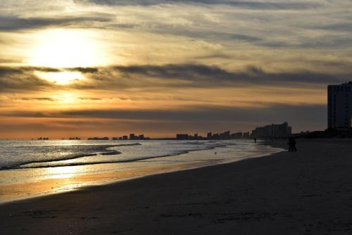 een persoon die bij zonsondergang op het strand loopt bij Yacht Club Villas #1-202 condo in Myrtle Beach