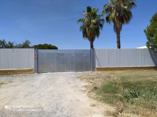 a white fence with two palm trees behind it at Casa rural la noria in Los Palacios y Villafranca