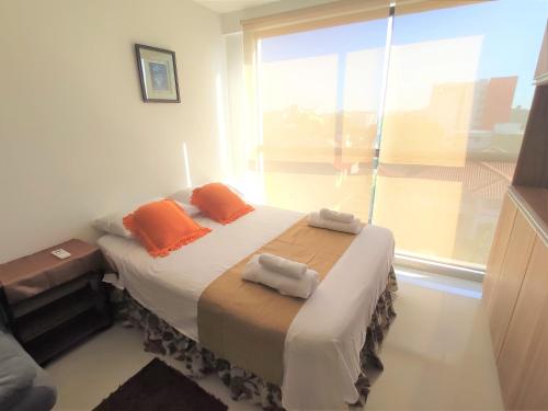 1 dormitorio con 1 cama con almohadas de color naranja y ventana en Departamento Inzio, Cómodo y Confortable, en Santa Cruz de la Sierra