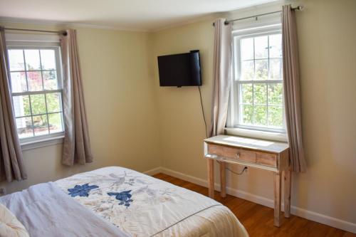 a bedroom with a bed and a television and two windows at Seaside Serenity, just a block /0.1 mile away from the beach in Yarmouth