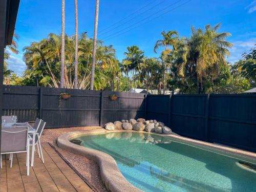 a swimming pool in a backyard with a fence and trees at Port Douglas Beach Cottage in Port Douglas