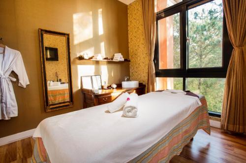 a bedroom with a bed with white sheets and a window at Dalat Edensee Lake Resort & Spa in Da Lat