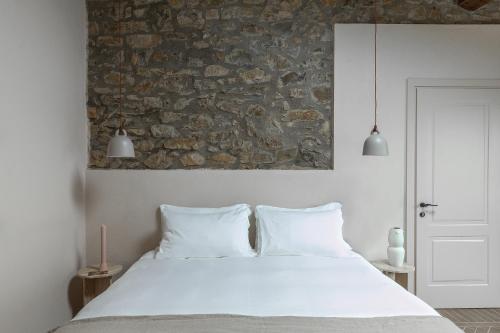 una camera con un letto bianco e un muro in pietra di Pieve Aldina Relais & Châteaux a Radda in Chianti