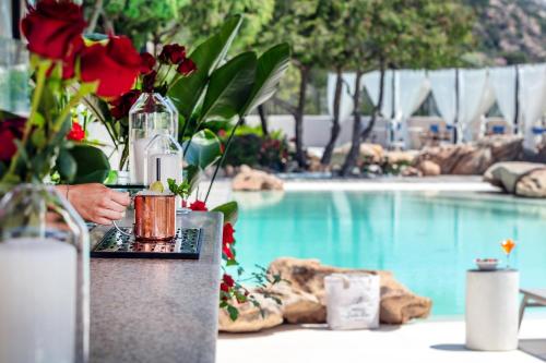a table with a drink and flowers next to a swimming pool at Hotel delle Rose a Luxury Boutique Hotel in Porto Cervo