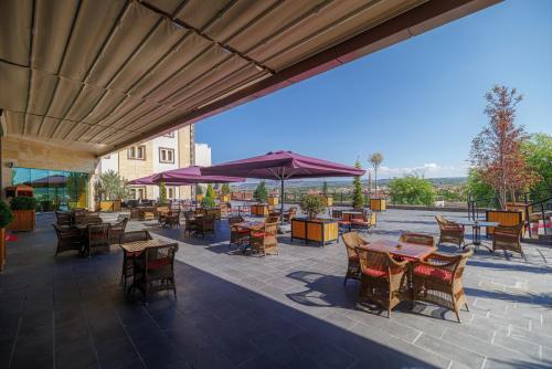 un patio con mesas, sillas y una sombrilla en Ramada By Wyndham Cappadocia, en Ortahisar