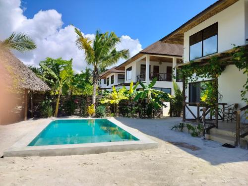 a villa with a swimming pool in front of a house at Sand Beach Boutique Villas in Bwejuu