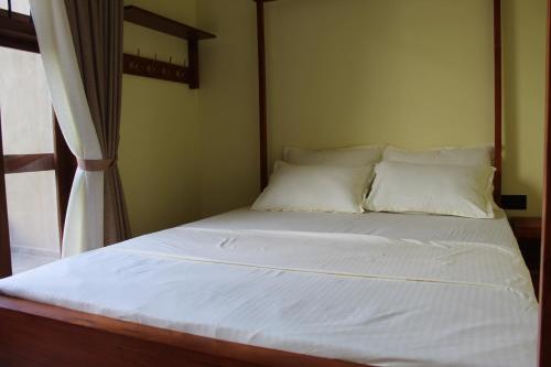 a bed with white sheets and pillows next to a window at Kandy Lotus Chalet in Kandy