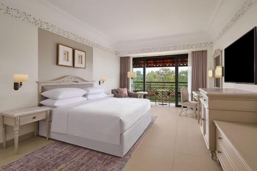 a white bedroom with a bed and a television at Mustika Yogyakarta Resort and Spa in Yogyakarta
