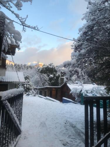 a snow covered yard with a house and trees at Cuatro Cerros Hostel in San Carlos de Bariloche