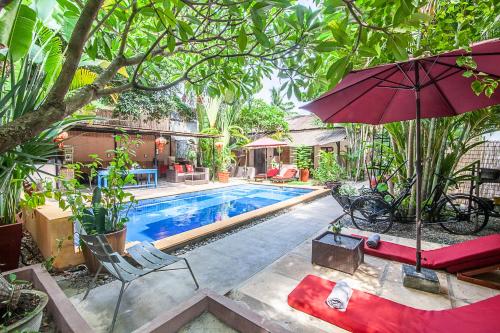 uma piscina com um guarda-sol vermelho e cadeiras e uma mesa em Maison 557 em Siem Reap