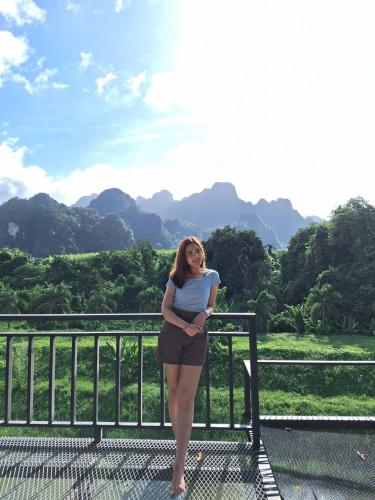 a woman standing next to a fence with mountains in the background at Phu Siab Mhok@KhaoSok in Khao Sok