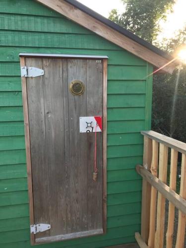 a green house with a wooden door on it at Tree house and shepherds hut in Ashburton