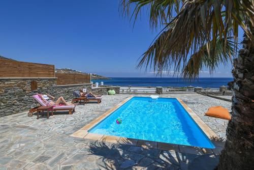 a swimming pool with people sitting in chairs next to the ocean at Santamare Villa in Tinos Town