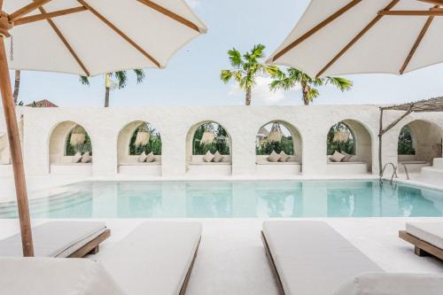a swimming pool with chairs and umbrellas at Hotel Sages in Canggu