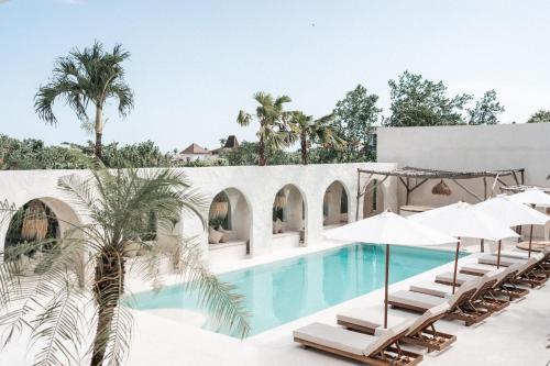 a swimming pool with lounge chairs and umbrellas at Hotel Sages in Canggu