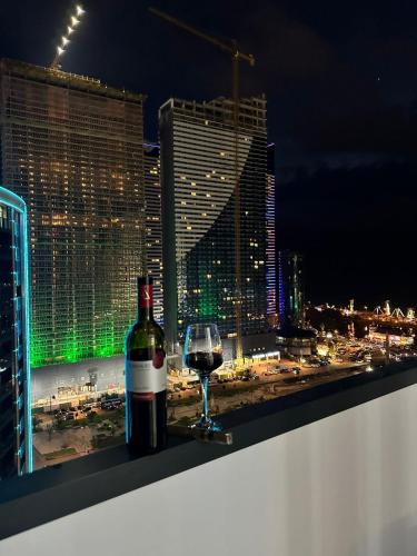 a bottle of wine and a glass on a ledge with a city skyline at Moonlight Apart-Hotel Batumi in Batumi