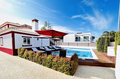 uma casa com piscina e guarda-sol vermelho em Romã do Meco na Aldeia do Meco