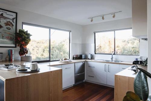 a kitchen with white cabinets and two large windows at Driftwood Rest Binalong Bay Sleeps 4 in Binalong Bay