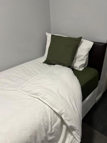a bed with white sheets and green pillows at Mona's Home in Dagenham